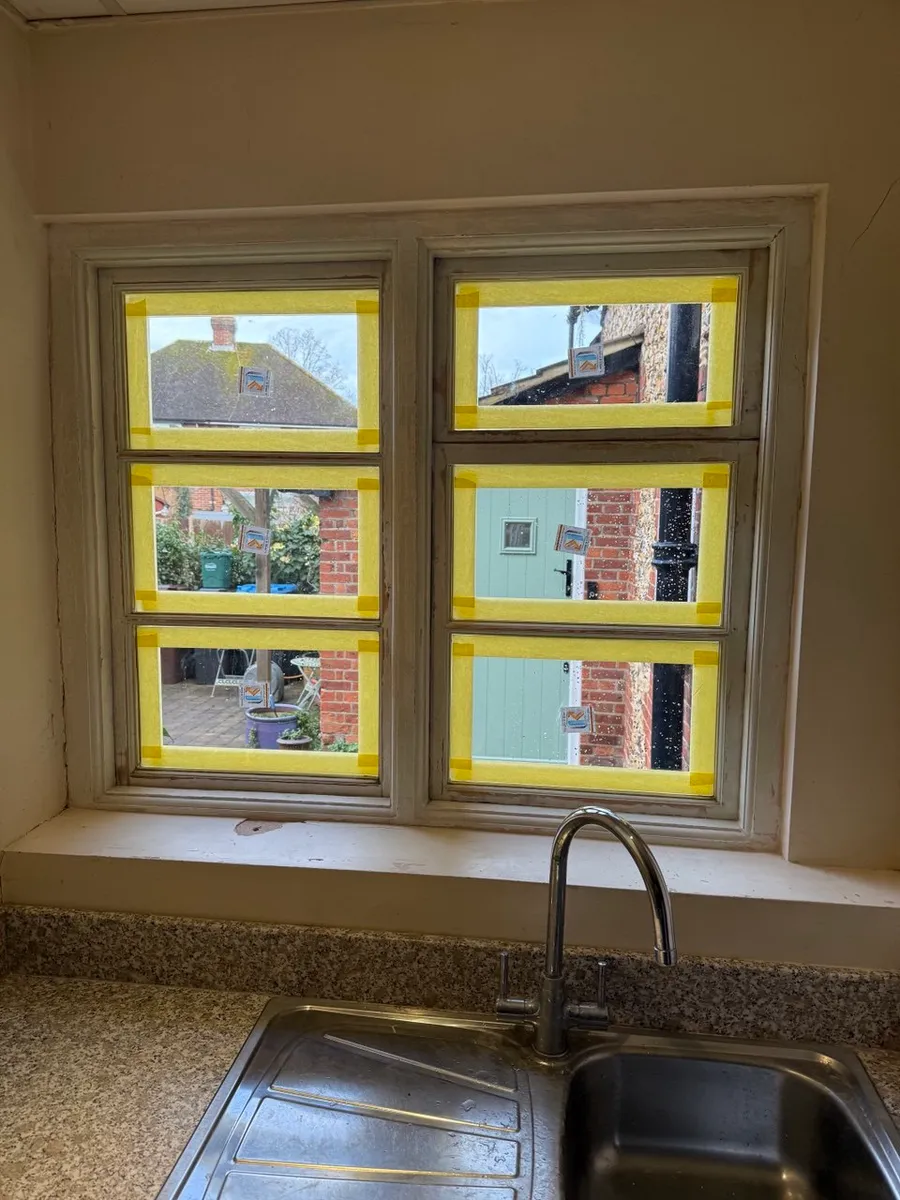 Cottage kitchen casement window over a sink with six panes masked off ready for repainting