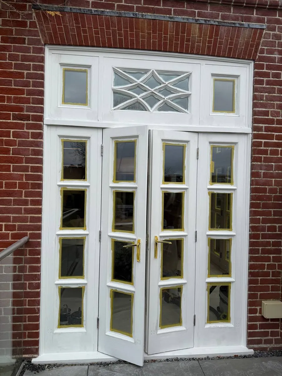 Restored white timber French doors with decorative leaded fanlight on a brick house