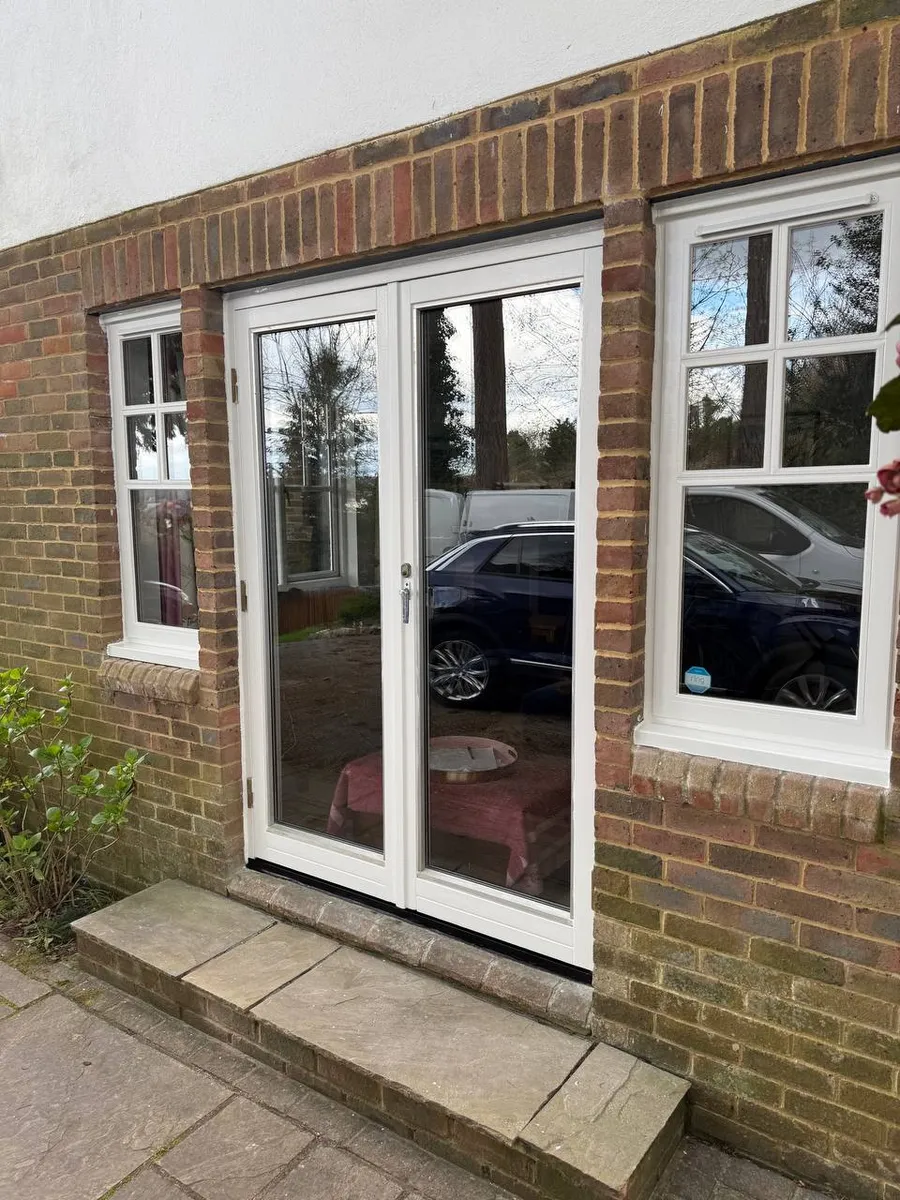 Restored white timber french doors with side casement windows on a brick house, Surrey