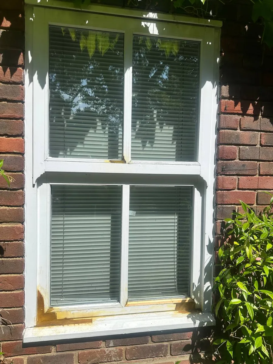 Restored timber sash window with fresh primer and new sill on a red brick wall in sunshine